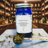 Blue jar labeled 'Chamomile Flowers' with a spoonful of dried chamomile flowers on a patterned background.