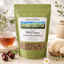 Load image into Gallery viewer, A green stand-up pouch of One Love Tea Wild Cherry with Lions Mane Mushroom loose leaf wellness tea, displayed on a wooden surface with cherries, a glass of amber tea, and sea urchin in a softly styled setting.